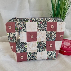 Puede incluir: Un neceser de patchwork con un estampado floral y detalles bordados. La bolsa tiene cierre de cremallera y una borla. La combinación de colores incluye tonos de rosa, blanco y verde oscuro.