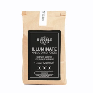 May include: A brown paper bag with a black label that says "HUMBLE SUDS ILLUMINATE MINERAL OXYGEN POWDER" and lists the ingredients as "3 HUMBLE INGREDIENTS: OXYGEN POWDER, WASHING SODA, BAKING SODA". The label also says "WHITENS & BRIGHTENS LIFTS STAINS & DEODORIZES" and "UNSCENTED". The bag is 40 oz and is compostable and recyclable.