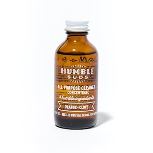 May include: A brown glass bottle with a white cap, labeled "HUMBLE SUDS ALL PURPOSE CLEANER CONCENTRATE 4 humble ingredients ORANGE + CLOVE 1.5 fl oz - REFILLS TWO 16oz OR ONE 32oz BOTTLE"