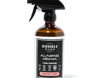 May include: A brown glass bottle with a black spray nozzle filled with all-purpose cleaner. The label reads "Humble Suds All Purpose Cleaner" and lists 5 humble ingredients: distilled water, grain alcohol, castile soap, grapefruit gel, and lemon oil. The bottle is labeled "Grapefruit - Lemon" and contains 16 fluid ounces.