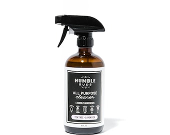 Puede incluir: Una botella de vidrio marrón con una boquilla de pulverización negra. La botella está etiquetada como "Humble Suds All Purpose Cleaner" con una lista de 5 ingredientes humildes y el aroma "Tea Tree - Lavender". La botella contiene 473 ml.