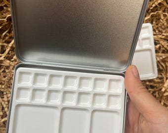 Puede incluir: Una paleta de pintura de metal plateado con un inserto de porcelana blanca. El inserto tiene 15 pozos individuales para pintura, incluidos tres pozos más grandes.