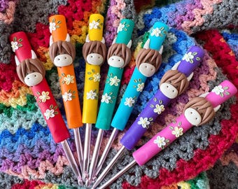 May include: Set of seven colorful crochet hooks with cute clay animal toppers. The hooks are arranged in a rainbow pattern, with each hook featuring a different animal topper. The hooks are on a rainbow crochet blanket.