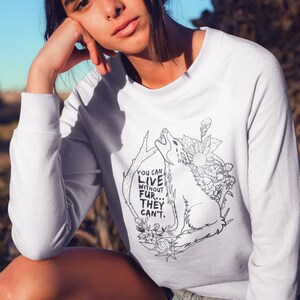 Puede incluir: Sudadera blanca con una ilustración en blanco y negro de un lobo aullando a la luna. El texto "You can live without fur... they can't." está impreso en la sudadera.