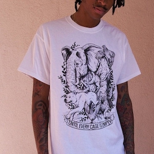 May include: A person wearing a white t-shirt with a black and white graphic of an elephant and other animals. The shirt has the text "Until Every Cage Is Empty" printed on it. The person is wearing blue jeans and white sneakers.