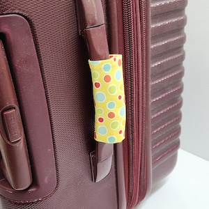 May include: A burgundy suitcase with a zipper and a handle covered in a yellow fabric with colourful polka dots.
