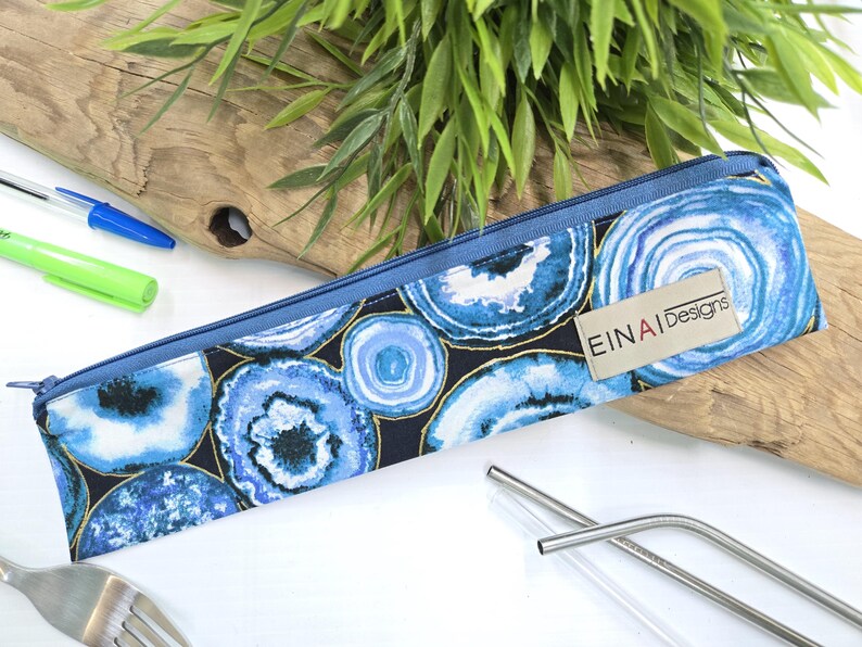 May include: A blue and gold zippered pouch with a pattern of blue agate slices. The pouch has a label that reads 'EINAI Designs'.