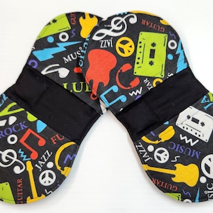 May include: Two black pot holders with a musical theme. The pot holders are decorated with colourful musical notes, guitars, peace signs, and cassette tapes. The text on the pot holders includes "Guitar", "Jazz", "Rock", "Music", and "Flu".