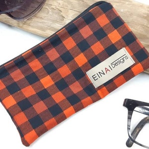 May include: Orange and black checkered glasses case with a zipper closure. The case has a label that reads "EINAI Designs".