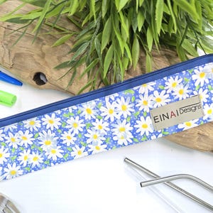 May include: A blue zippered pouch with a white daisy pattern. The pouch has a brown label with the text 'EINAI Designs'.
