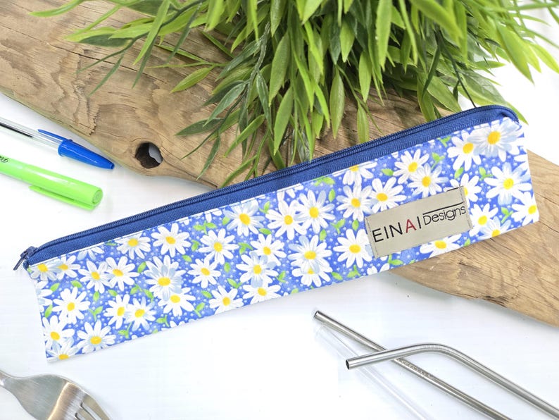 May include: A blue zippered pouch with a white daisy pattern. The pouch has a brown label with the text 'EINAI Designs'.