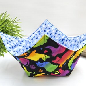 May include: A black fabric bowl with a rainbow cat print and a blue paw print lining. The bowl is folded and ready to be used.