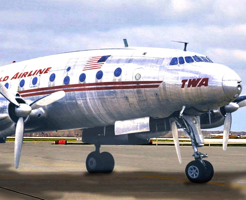May include: A silver Lockheed Constellation airplane with red and blue stripes and the words "TWA" and "World Airline" on the side. The airplane is on a runway with a cloudy sky in the background.