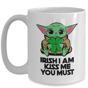 Puede incluir: Taza de cer&aacute;mica blanca con un personaje de dibujos animados verde sosteniendo un tr&eacute;bol de cuatro hojas. El texto en la taza dice "Irish I am Kiss Me You Must".