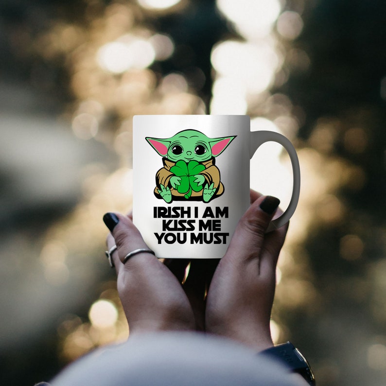 Puede incluir: Taza de cer&aacute;mica blanca con un personaje de dibujos animados verde sosteniendo un tr&eacute;bol. El texto en la taza dice "Irish I am Kiss Me You Must".