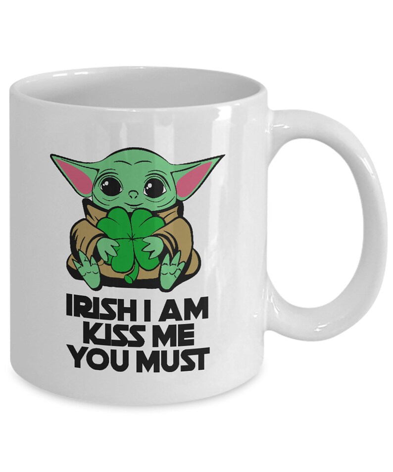 Puede incluir: Taza de cer&aacute;mica blanca con un personaje de dibujos animados verde que sostiene un tr&eacute;bol de cuatro hojas. El texto "IRISH I AM KISS ME YOU MUST" est&aacute; impreso en la taza.