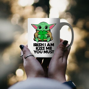Puede incluir: Taza de cer&aacute;mica blanca con un personaje de dibujos animados verde sosteniendo un tr&eacute;bol. La taza tiene el texto "Irish I am Kiss Me You Must" impreso en ella.