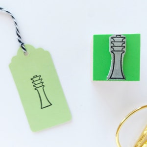 Op de afbeelding: Een groene rubberen stempel met een zwart-witte illustratie van een toren. Een groen label met een zwart-witte illustratie van een toren. Een gouden schaar met zwarte handvatten.