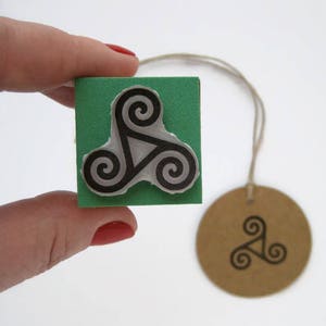 May include: A green rubber stamp with a black and white Celtic knot design. The stamp is on a white surface.