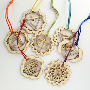 May include: A collection of seven laser-cut wooden ornaments, each featuring a unique geometric or symbolic design. These circular pendants are suspended by colorful cords in shades of orange, yellow, green, teal, purple, and blue, with intricate cutouts.