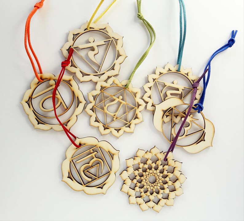 May include: A collection of seven laser-cut wooden ornaments, each featuring a unique geometric or symbolic design. These circular pendants are suspended by colorful cords in shades of orange, yellow, green, teal, purple, and blue, with intricate cutouts.