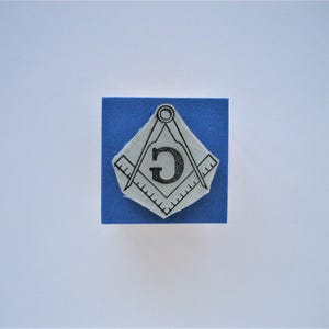May include: A blue square with a white image of a compass and square with the letter "G" in the center.