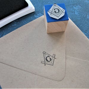 May include: A wooden block with a blue top and a black and white image of a compass and the letter "G" on it. The block is sitting on a blue and white patterned surface.