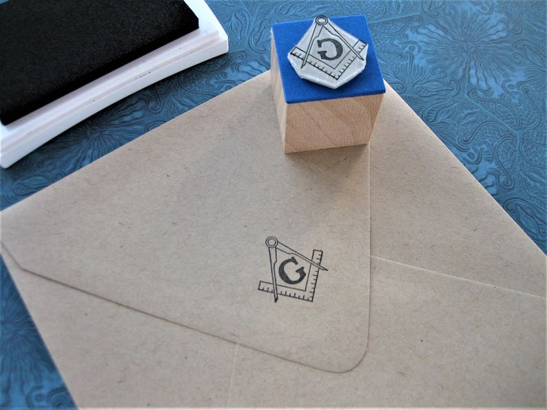May include: A wooden block with a blue top and a black and white image of a compass and the letter "G" on it. The block is sitting on a blue and white patterned surface.