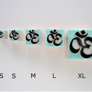 May include: Five wooden rubber stamps with a turquoise blue background and a black Om symbol. The stamps are arranged in a row from smallest to largest, labeled XS, S, M, L, and XL.