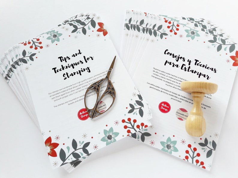 May include: A stack of white cards with a red and green floral pattern. The cards have the text "Tips and Techniques for Stamping" and "Consejos y T&eacute;cnicas para Estampar" printed on them. A pair of scissors and a wooden stamp are also in the image.