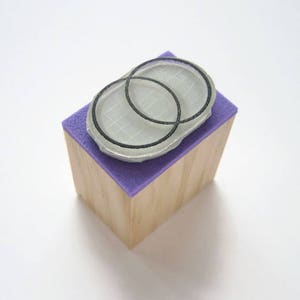 Op de afbeelding: Een houten blok met een paarse oppervlak en een rubberen stempel met twee overlappende cirkels erop.