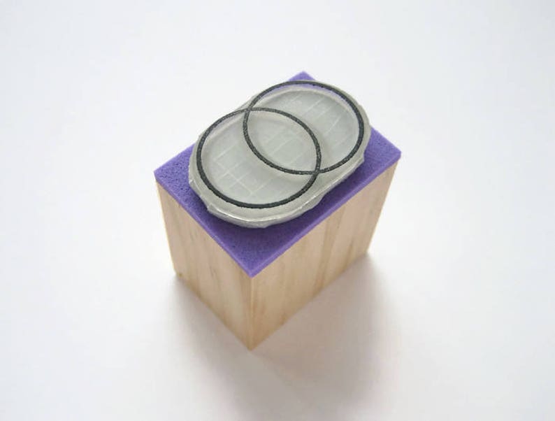 Op de afbeelding: Een houten blok met een paarse oppervlak en een rubberen stempel met twee overlappende cirkels erop.