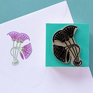 May include: A rubber stamp with a black design of three stylized lotus flowers on a turquoise background. The stamp is mounted on a wooden block.