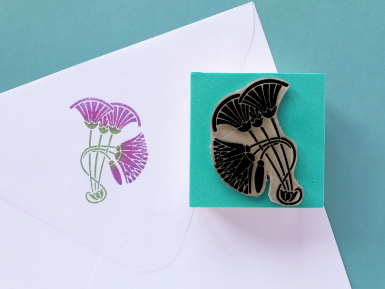 May include: A rubber stamp with a black design of three stylized lotus flowers on a turquoise background. The stamp is mounted on a wooden block.