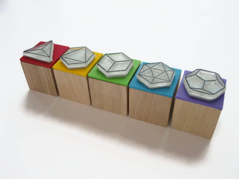 May include: Six wooden blocks with different geometric shapes on top. The blocks are painted in a rainbow of colors, starting with red and ending with purple.