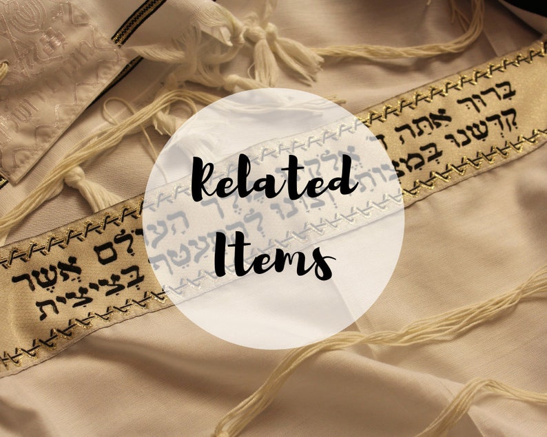 May include: A white tallit prayer shawl featuring a gold-colored atarah band embroidered with black Hebrew text. The garment includes white tzitzit fringes at the corners and a semi-transparent circular overlay with the text Related Items.