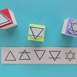 May include: Five wooden stamps with different geometric designs. The stamps are red, yellow, purple, and brown. The designs include a triangle, a star, and a circle. The stamps are arranged in a row on a blue surface.