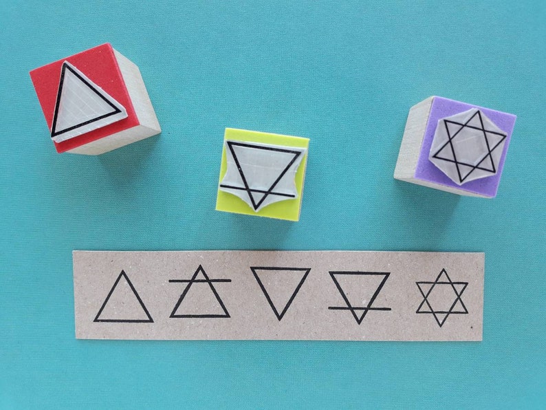 May include: Five wooden stamps with different geometric designs. The stamps are red, yellow, purple, and brown. The designs include a triangle, a star, and a circle. The stamps are arranged in a row on a blue surface.