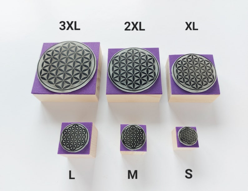 May include: Six wooden blocks with purple tops and a black and white flower of life design. The blocks are labeled with sizes: 3XL, 2XL, XL, L, M, and S.