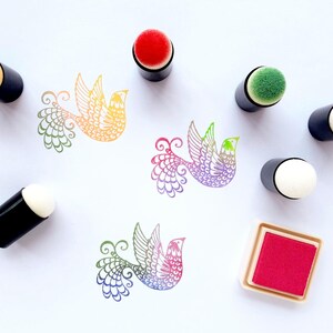 May include: An assortment of colorful bird stamps and ink pads. The stamps are in the shape of birds with intricate wing and tail designs. The ink pads are red and the stamp applicators have black handles with various colored sponge tips.