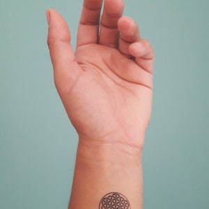 Op de afbeelding: Een close-up van iemands pols met een zwart-witte levensbloem tatoeage.