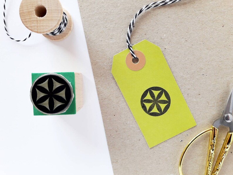 Op de afbeelding: Een geel cadeau-etiket met een geometrisch ontwerp in zwart en wit. Het etiket is vastgebonden met touw en heeft een bruine papieren cirkel bevestigd.