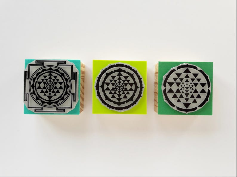 May include: Three square stamps with wooden bases and colored tops in teal, lime green, and forest green. Each stamp features a black Sri Yantra geometric design printed on a circular or square silver-toned plate attached to the top surface.