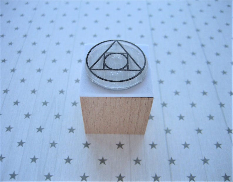 May include: A wooden block stamp with a clear, round, geometric design. The design features a triangle with a circle inside.