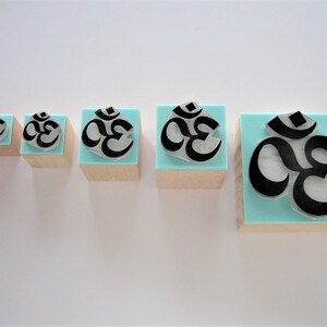 May include: Five wooden blocks with a blue background and a black Om symbol. The blocks are arranged in a row from smallest to largest.