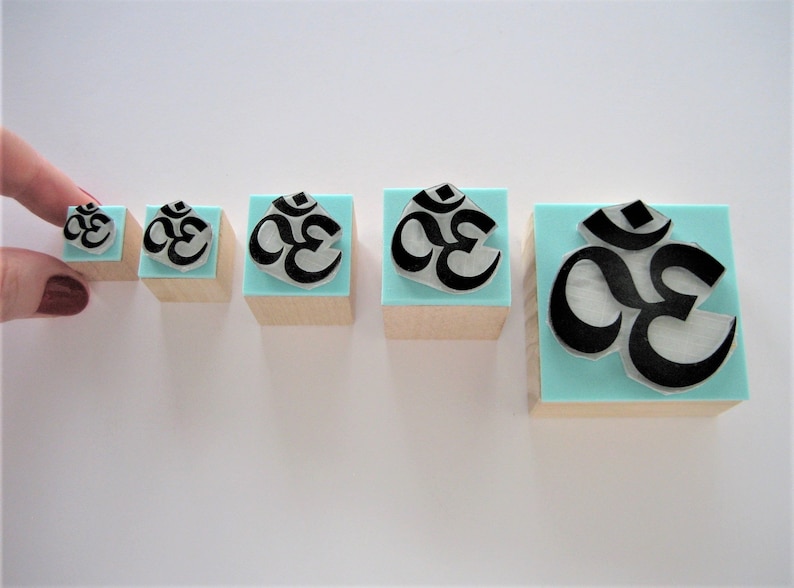 May include: Five wooden blocks with a blue background and a black Om symbol. The blocks are arranged in a row from smallest to largest.