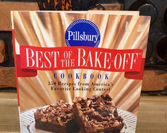 May include: A Pillsbury cookbook titled "Best of the Bake-Off Cookbook" featuring 350 recipes from America's Favorite Cooking Contest. The cover features a photo of two chocolate brownies with chocolate chips and nuts on a white plate. The text "Featuring the $1,000,000 Grand Prize Recipe" is on the cover.