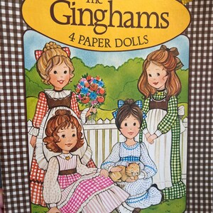 May include: A vintage Whitman paper doll book featuring four girls in gingham dresses. The book cover has a yellow title bar with the text "The Ginghams 4 Paper Dolls".