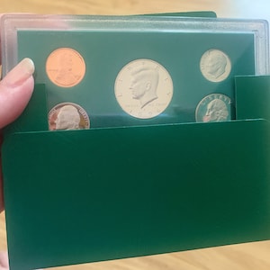 May include: A 1996 United States Mint coin set in a green protective folder. The set includes a penny, nickel, dime, quarter, and a Kennedy half dollar. The coins are displayed against a green background within a clear plastic case.