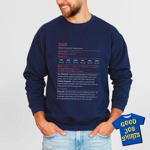 May include: Navy blue sweatshirt with the word "DAD" and a humorous role-playing game-style description. The text includes stats, skills, and actions. A small blue t-shirt with "GOOD JOB SHIRTS" is in the lower right corner.